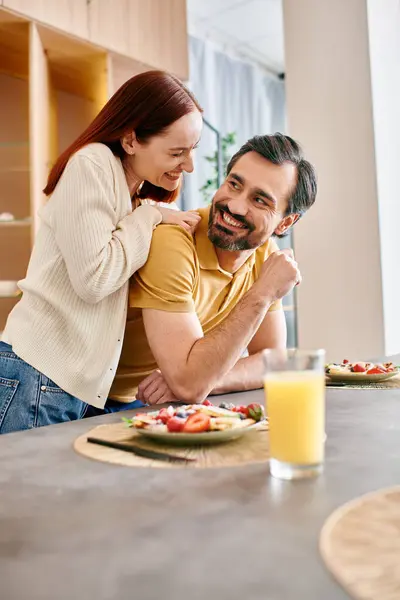 A bearded man and a redhead woman joyfully eating breakfast together in their modern kitchen. — Stock Photo