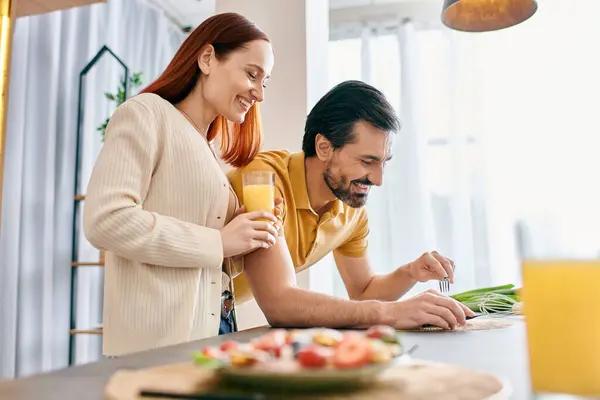 A redhead woman and bearded man cook a meal together in a modern kitchen, sharing a special moment preparing food. — Stock Photo