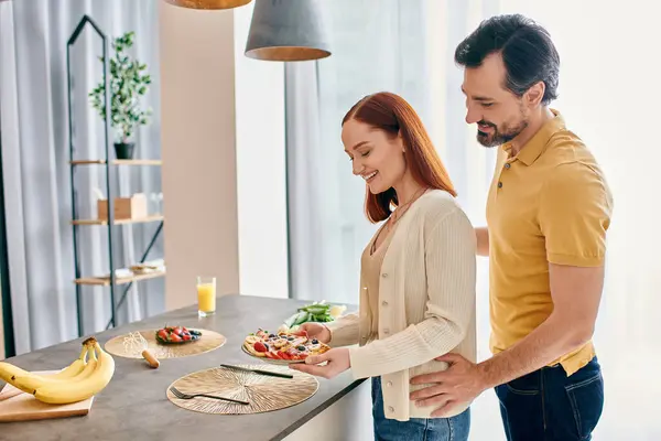 Рыжая женщина и бородатый мужчина радостно готовят еду вместе на современной кухне, соединяясь с искусством приготовления пищи.. — стоковое фото