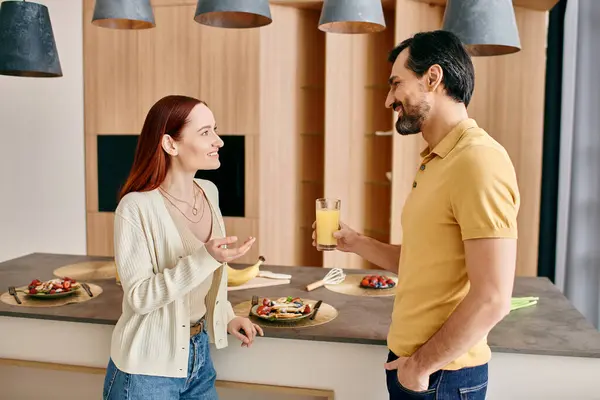 A redhead woman and bearded man talk in a modern kitchen, enjoying quality time together. — Stock Photo