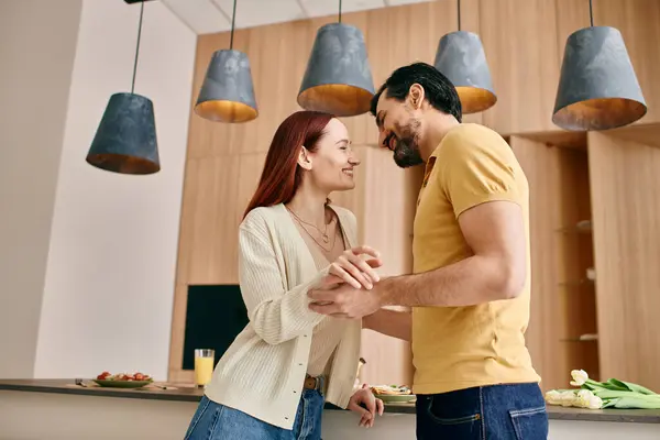 A beautiful adult couple, a redhead woman and a bearded man, standing together in a modern kitchen, spending quality time. — Stock Photo