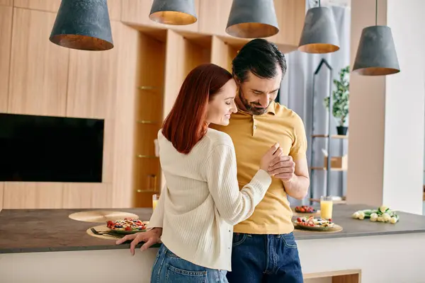 Un uomo barbuto e una donna rossa stanno insieme in una cucina moderna, mostrando tempo di qualità trascorso a cucinare e legare. — Foto stock