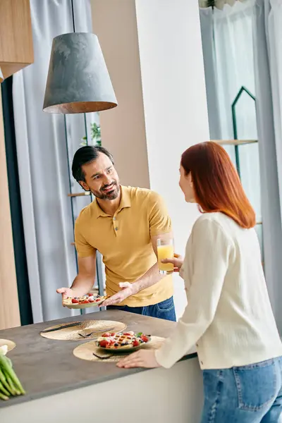 A redhead woman and bearded man in a modern kitchen, passionately preparing food together with love and laughter. — Stock Photo