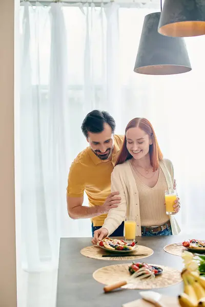 A beautiful adult couple, the woman with red hair and the man with a beard, are enjoying breakfast together in a modern kitchen. — Stock Photo