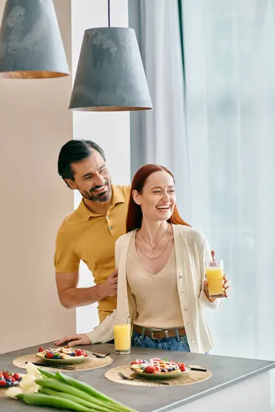 A redhead woman and a bearded man are enjoying breakfast together in their modern kitchen. — Stock Photo