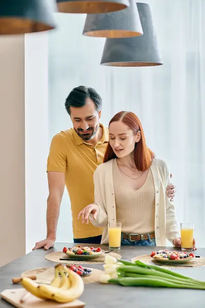 A redhead woman and bearded man sit at a kitchen table, laughing and enjoying breakfast together in a modern apartment. — Stock Photo