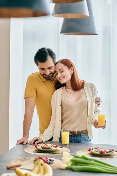 A beautiful adult couple, a redhead woman and a bearded man, strike a pose in a modern kitchen with food on the counter. — Stock Photo
