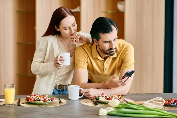 A redhead woman and bearded man engrossed in their phones while sharing breakfast in a modern apartment. — Stock Photo
