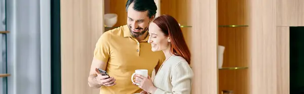 A bearded man and a redhead woman engrossed in their phone, sharing a moment of digital connection in their modern apartment. — Stock Photo