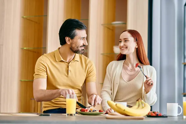 A bearded man and a redhead woman enjoy a cozy breakfast together in a modern kitchen, creating a warm and harmonious scene. — Stock Photo