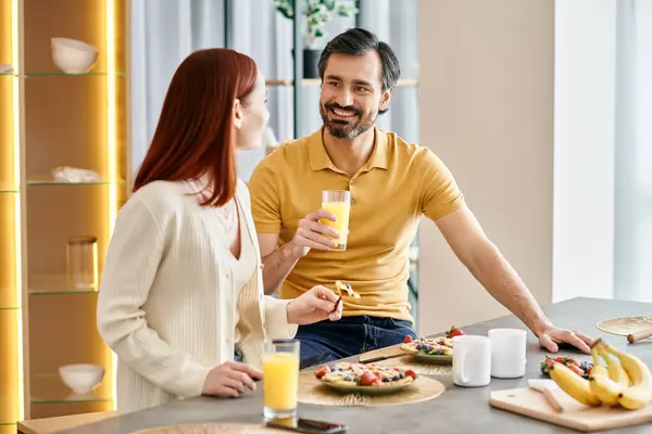 Рыжая женщина и бородатый мужчина ценят время вместе, наслаждаясь апельсиновым соком за их кухонным столом.. — стоковое фото