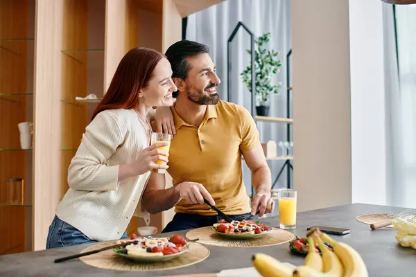Рыжая женщина и бородатый мужчина наслаждаются едой вместе на современной кухне, создавая уютную и интимную атмосферу. — стоковое фото