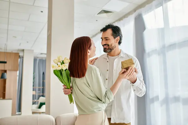 A man with a beard is giving a gift to a beautiful redhead woman in a stylish living room. — Stock Photo