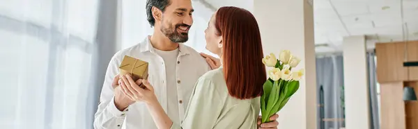 A bearded man in a modern apartment offers a bouquet of flowers to his redhead woman, creating a sweet and romantic moment. — Stock Photo