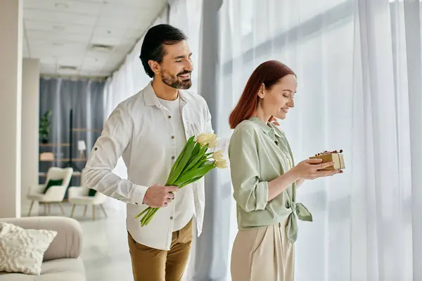 Redhead woman and bearded man standing in modern living room, holding flowers. — Stock Photo