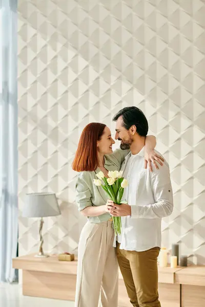 A redhead woman and bearded man stand in front of a wall with flowers in a modern apartment, enjoying quality time together. — Stock Photo