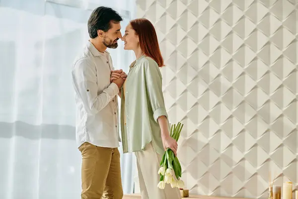 A redheaded woman and a bearded man standing in front of a wall adorned with vibrant flowers, sharing a moment of connection. — Stock Photo