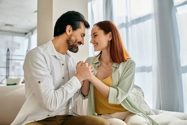 Ein schönes erwachsenes Paar, eine rothaarige Frau und ein bärtiger Mann sitzen zusammen auf einer Couch in einem modernen Appartement und genießen die schöne Zeit. — Stockfoto