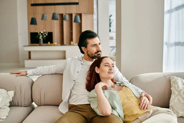 Una mujer pelirroja y hombre barbudo disfrutando de la compañía de los demás en un cómodo sofá en una elegante sala de estar. — Stock Photo