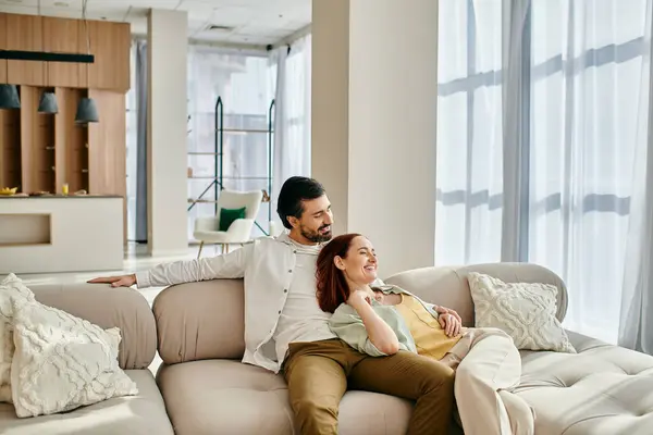 Um homem e uma mulher, uma ruiva e um homem barbudo, relaxam em um sofá em uma sala de estar moderna, desfrutando de tempo de qualidade juntos. — Fotografia de Stock