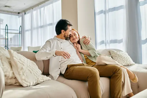 A redhead woman and a bearded man sit on a cozy couch, sharing a moment of peace and connection in their modern living room. — Stock Photo