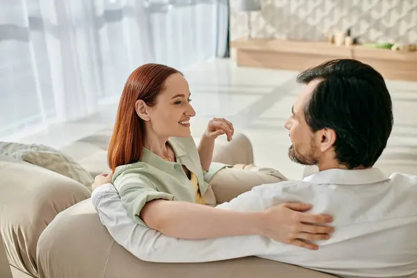 Красивая взрослая пара, рыжая женщина и бородатый мужчина, расслабьтесь и поговорите на диване в современной гостиной. — стоковое фото