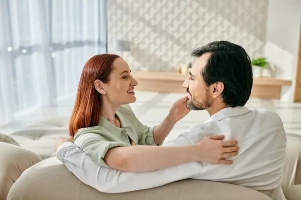 Un beau couple d'adultes, une rousse et un homme barbu, s'assoient étroitement sur un canapé dans leur salon moderne. — Photo de stock