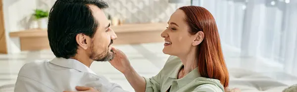 A redhead woman and bearded man share a tender moment as they gaze into each others eyes in a modern apartment. — Stock Photo