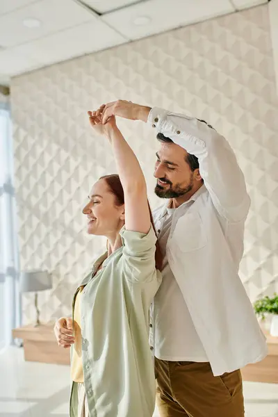Ein bärtiger Mann und eine rothaarige Frau tanzen fröhlich in einem Büroambiente und bringen Leben und Energie in den Arbeitsplatz. — Stockfoto
