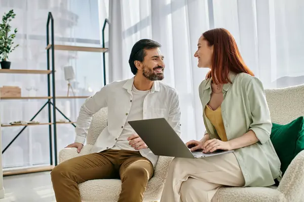 Una rossa e un uomo barbuto sono seduti insieme, concentrandosi su uno schermo del computer portatile mentre trascorrono del tempo di qualità a casa.. — Foto stock