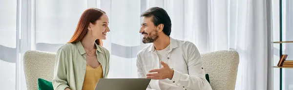 Un uomo barbuto e una donna rossa impegnati in una conversazione profonda mentre seduti comodamente su un divano moderno in un accogliente appartamento. — Foto stock