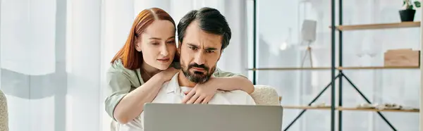 A bearded man and a redhead woman sit on a couch, focused on a laptop screen in their modern apartment. — Stock Photo