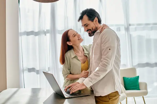 Una hermosa pelirroja y un hombre barbudo están sentados juntos, utilizando un ordenador portátil en su apartamento moderno. — Stock Photo