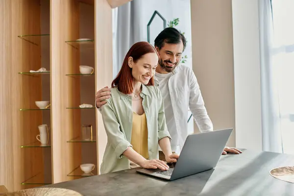 A couple, the woman with red hair and the man with a beard, engrossed in a laptop, bonding in their modern apartment. — Stock Photo