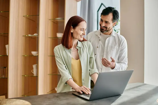 A redhead woman and bearded man engaged with a laptop in a stylish kitchen, deep in conversation and bonding together. — Stock Photo