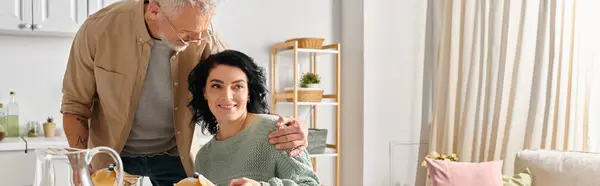 Un hombre está al lado de su esposa discapacitada, ambos conversando felizmente mientras están en la cocina de su casa. - foto de stock