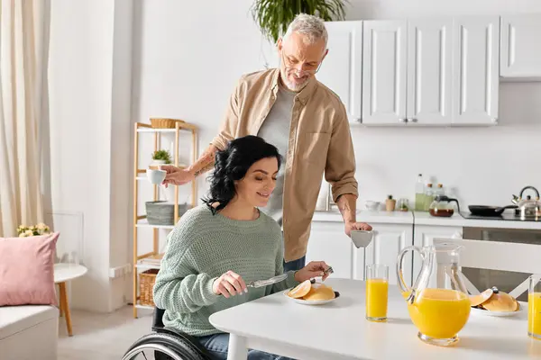 Una mujer discapacitada en silla de ruedas y su marido cocinando juntos en su cocina en casa. - foto de stock