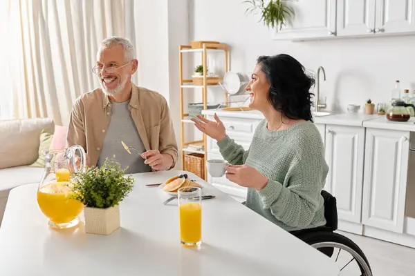 A man and a woman, the woman in a wheelchair, engaged in conversation at a table in a cozy kitchen setting. — Stock Photo