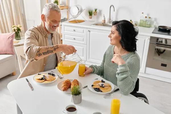 Una donna disabile in sedia a rotelle e suo marito gustare la colazione insieme a un tavolo da cucina nella loro casa accogliente. — Foto stock