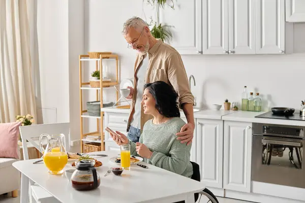 A man and a disabled woman in a wheelchair together in a cozy kitchen at home, sharing a warm moment. — Stock Photo