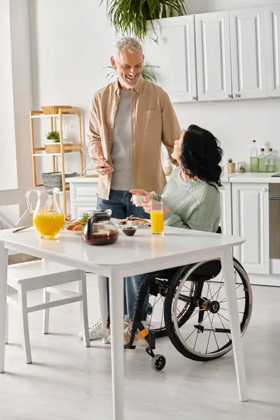 Uma mulher em uma cadeira de rodas conversando com um marido em uma cozinha em casa. — Fotografia de Stock