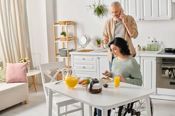 A husband and disabled wife in a wheelchair, stand side by side at a kitchen table, creating a heartwarming scene. — Stock Photo