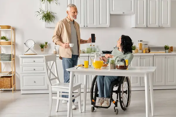 A disabled woman in a wheelchair having a conversation with her husband in a cozy kitchen at home. — Stock Photo