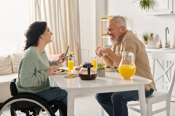 A man and woman in wheelchair engaged in conversation in a domestic kitchen setting. — Stock Photo