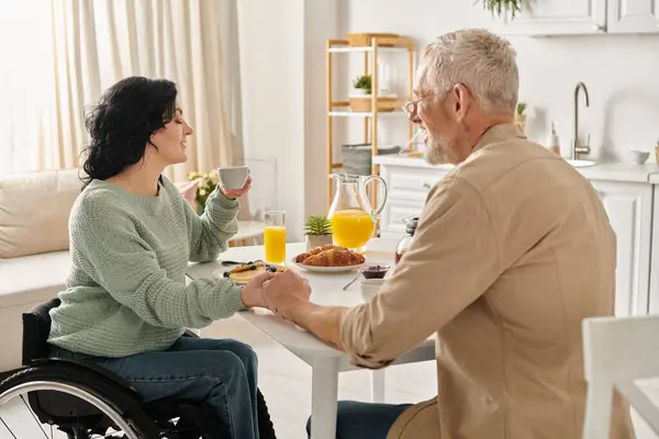 Une femme handicapée en fauteuil roulant profite d'un moment avec son mari à une table de cuisine dans leur maison. — Photo de stock