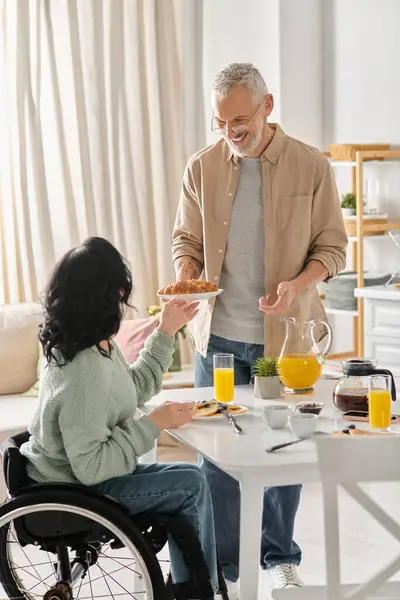 A man and a woman in wheelchair enjoying a meal together in their kitchen at home. — Stock Photo