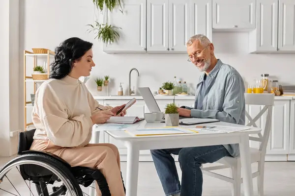 A woman in a wheelchair and her husband using a laptop in the kitchen at home. — Stock Photo