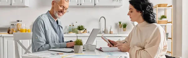 A man and woman work on a laptop at a kitchen table in the comfort of their home. — Stock Photo