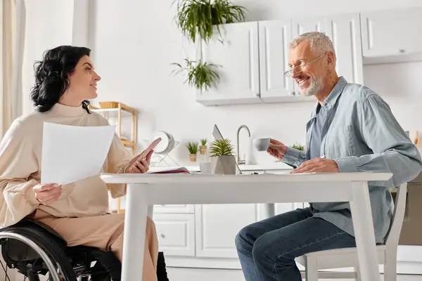 Um homem em uma cadeira de rodas se envolve em conversa com uma mulher em uma cozinha em casa. — Fotografia de Stock