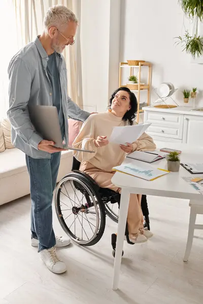 Una mujer discapacitada en silla de ruedas y su marido en silla de ruedas trabajan juntos alegremente en su cocina en casa. - foto de stock
